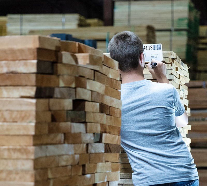 Granite Valley Forest Products employee seen from behind while marking lumber with a marker