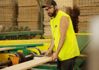 a worker in a sleeveless shirt holds one end of a board