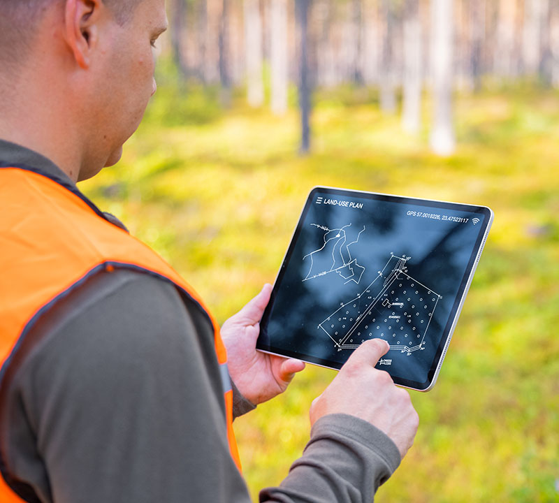 A forester in the woods looking at a land use plan on a tablet